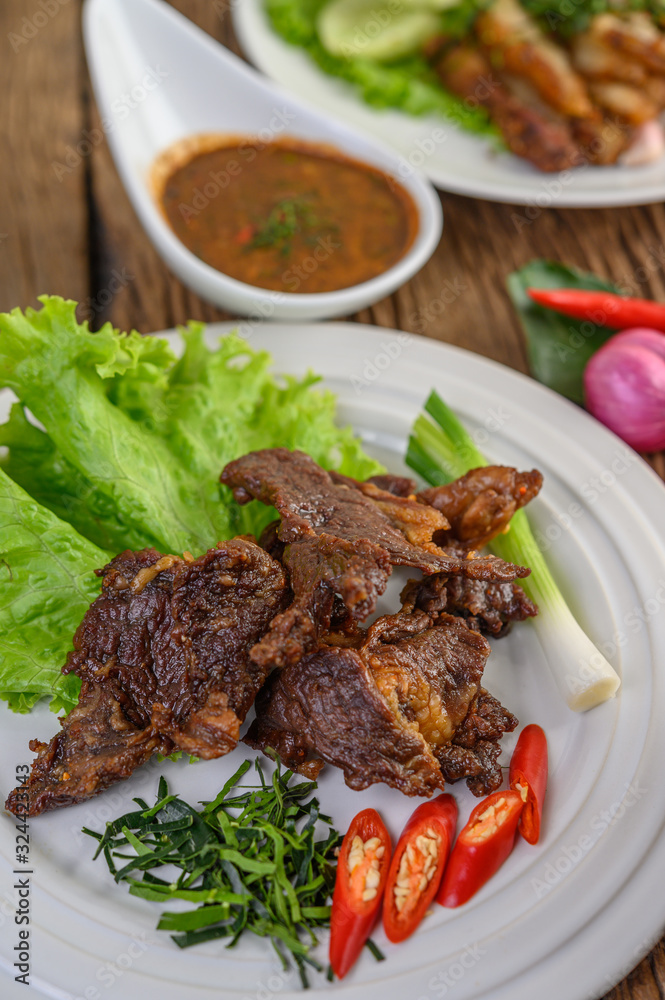 Beef fried Thai food on a white plate with spring onion, kaffir lime leaves, chilies, salad and chili paste in a cup.