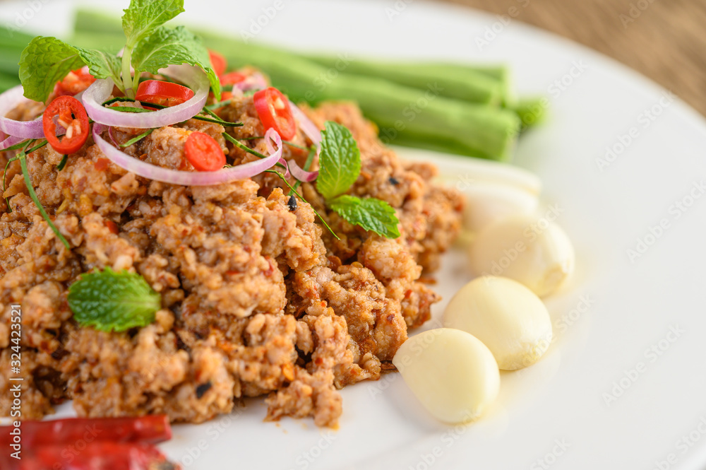Spicy Minced Pork Salad on a white plate with lentils, kaffir lime leaves and spring onions.