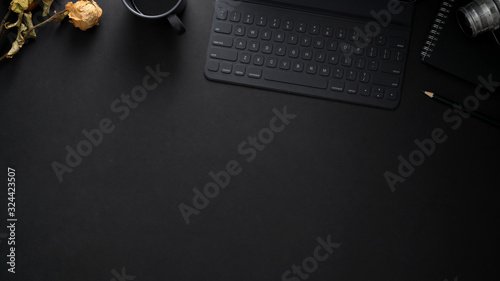 Top view of  workplace with wireless keyboard, copy space, camera and dry roses on black table