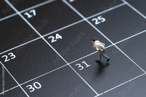 Business schedule plan, travel date or end of month pay day for salary man concept, miniature people businessman figure with suitcase walking on 31 end of month calendar