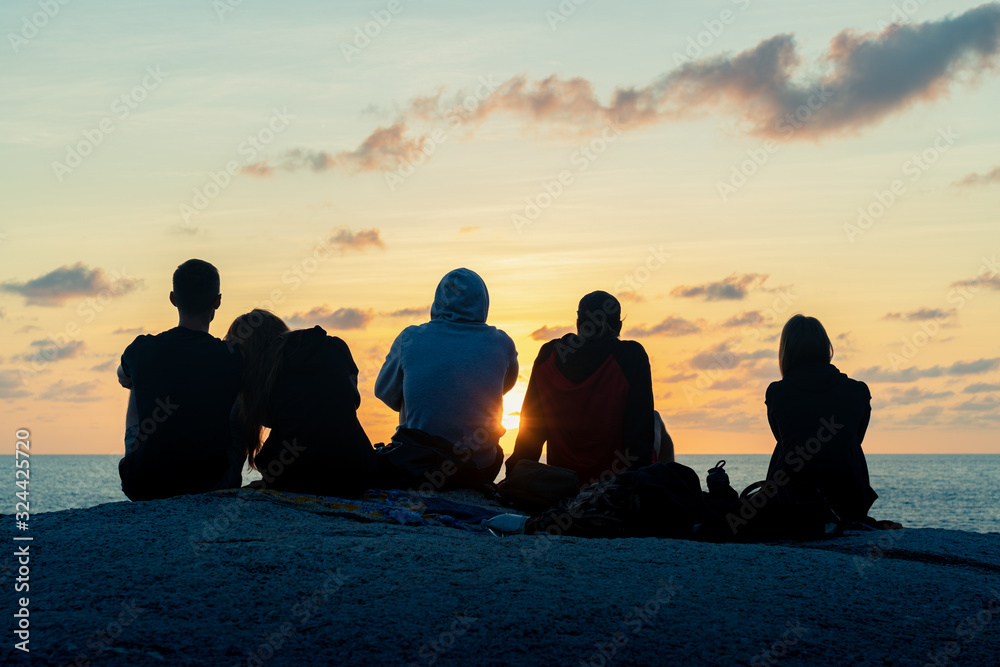 A group of young guys and girls meets dawn on a rock by the sea 