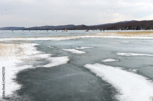 Melting snow with ice on the Big Lake with fishermen in the distance in the spring. Krasnoyarsk region. Russia.