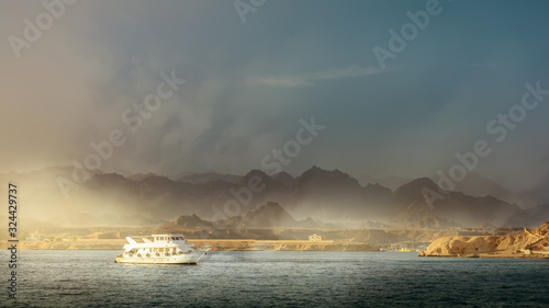Small pleasure motor boat sails on mountain background. Side view