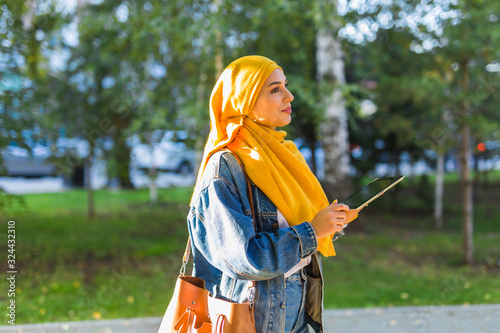 Arab woman student. Beautiful muslim female student wearing bright yellow hijab holding tablet.