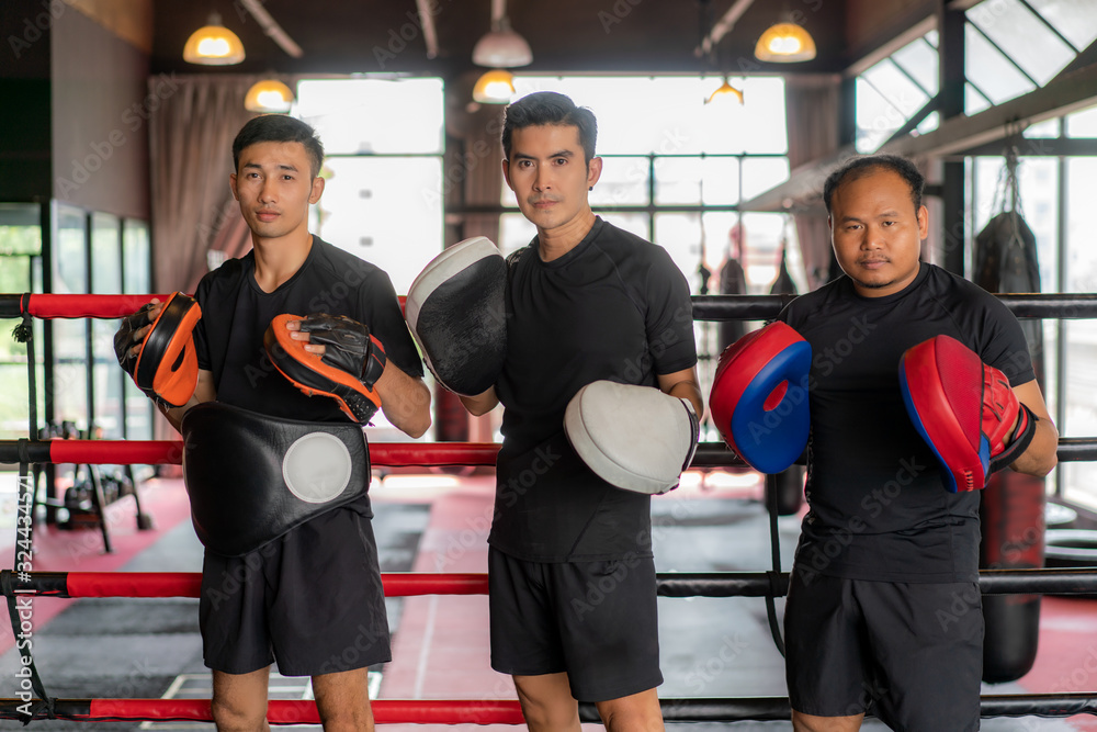 Three Asian boxer man looking at camera and pose and smile while leaned on black red ropes on boxing ring, and have a rest after hard training in black loft gym. Three Asian boxer man looking at camera and pose and smile while leaned on black red ropes on boxing ring, and have a rest after hard training in black loft gym.