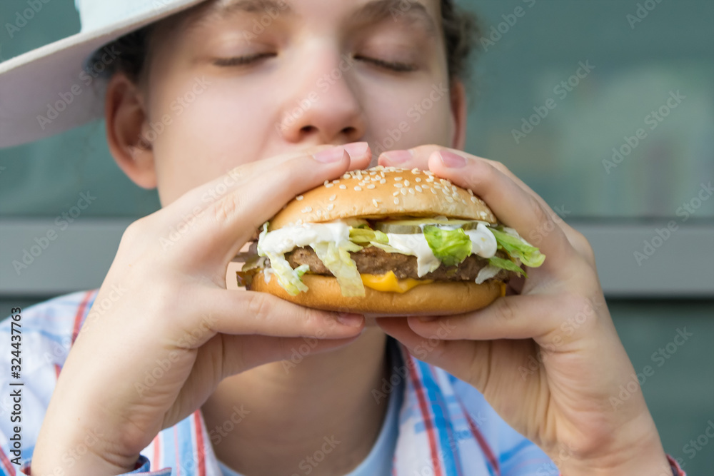 girl holding a big burger in her hands and bites it, closing her eyes with pleasure
