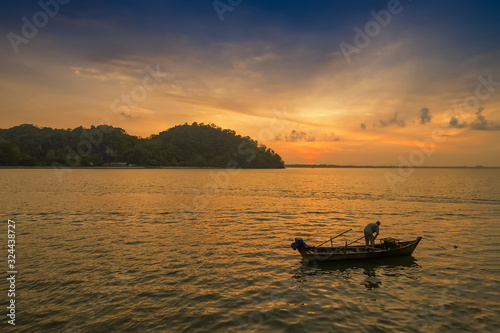 view seaside morning of a fisherman working in fishing boat floating in the sea with yellow sun light and blue sky background, sunrise at Mu Ko Phetra National Park, Satun, Thailand.
