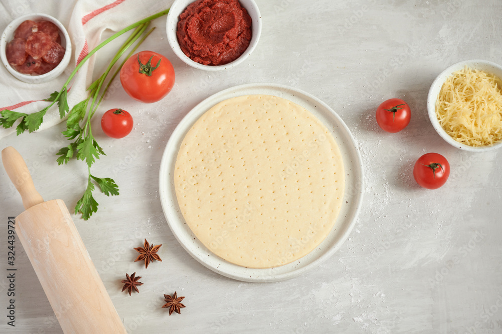 Fresh dough pizza base and ingredients on a white table. Top view. Fresh dough pizza base and ingredients on a white table. Top view.