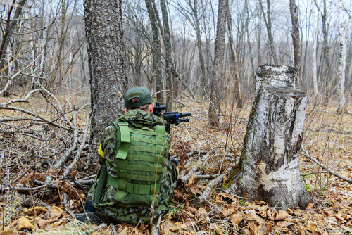 Man in uniform beside tree move with machine gun. Rear view.