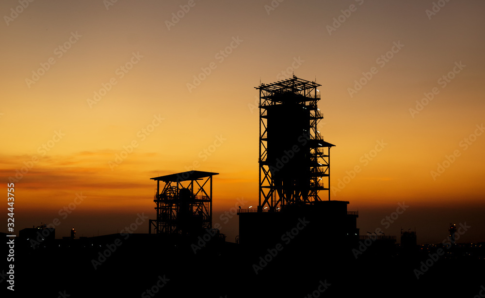 Oil refinery or chemical plant silhouette with night lights on at sunset.