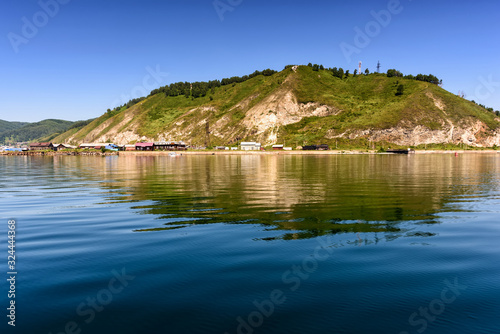 ake Baikal close to village Port Baikal, Russia. Horizontal day view of the high shore, green forest, houses, clear lake water