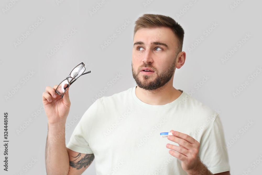 Thoughtful man with contact lens case and eyeglasses on grey background Thoughtful man with contact lens case and eyeglasses on grey background