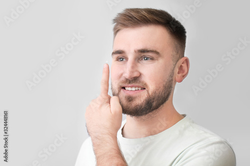 Young man putting in contact lenses on grey background