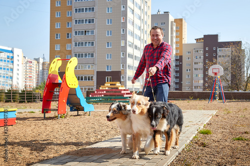 Photography Plump man with three dogs walking on children playground in city yard with big b