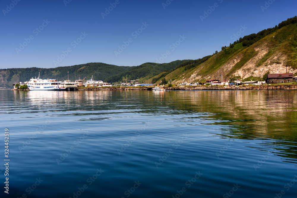 Lake Baikal close to village Port Baikal, Russia. Horizontal day view of the high shore, green forest, houses, ships, clear lake water