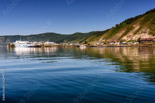 Lake Baikal close to village Port Baikal, Russia. Horizontal day view of the high shore, green forest, houses, ships, clear lake water