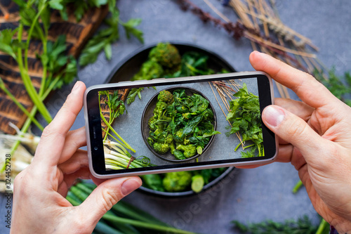 Take picture of food with phone at kitchen. Smartphone photo of green broccoli, spinach salad. Vegan healthy dietary food.