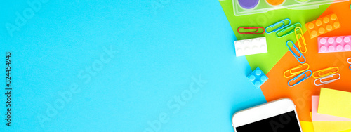 smart phone,plastic toy block,clipper,water color palete,pin,on blue background.flat lay, top view with banner ratio