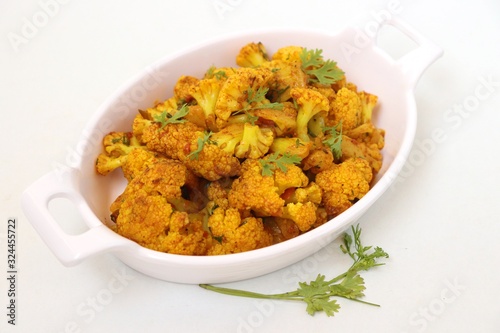 Dry cauliflower curry or Gobhi ki sabji or Gobi Masala served in white bowl with wooden spoons and coriander over white background with copy space.