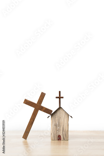 Wooden cross leaning on a small house wooden model on wooden board and white background photo
