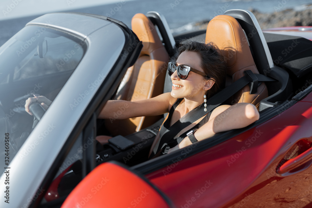 Young woman in swimsuit driving convertible car near the ocean, enjoying summer vacations while traveling on the island. Concept of a carefree travel and summer time