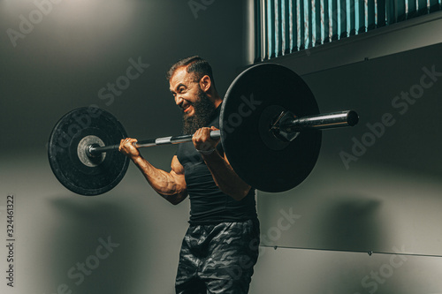 Muscular man in black sportswear lifting barbell in a gym