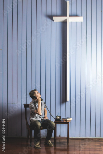 Caucasian man making a phone call looking at the white cross on wall. Concept trying to talk to god photo