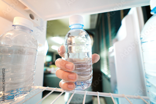 Photo Hand reaching into refrigerator taking a plastic bottle of water out