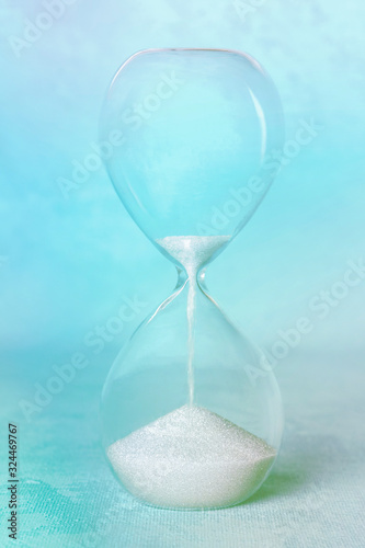 Time concept. An hourglass on an abstract background, with sand leaking through. Blue toned image