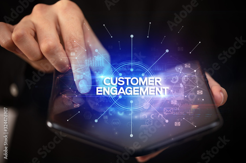 Businessman holding a foldable smartphone with CUSTOMER ENGAGEMENT inscription, new business concept