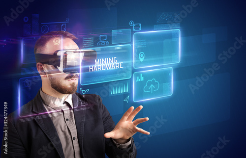Businessman looking through Virtual Reality glasses with MINING HARDWARE inscription, new technology concept