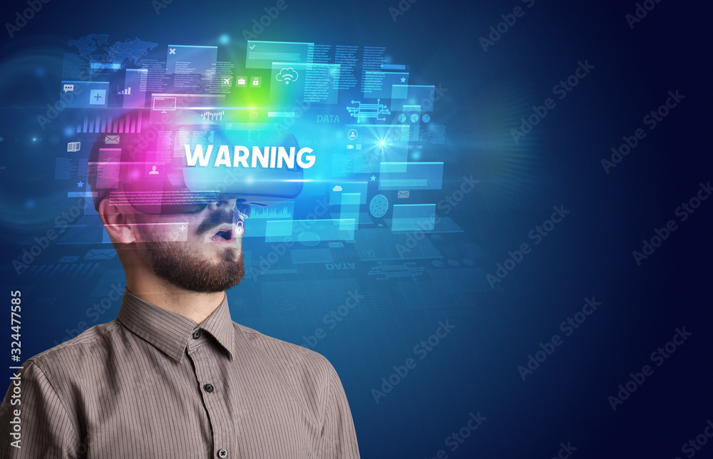 Businessman looking through Virtual Reality glasses with WARNING inscription, innovative security concept