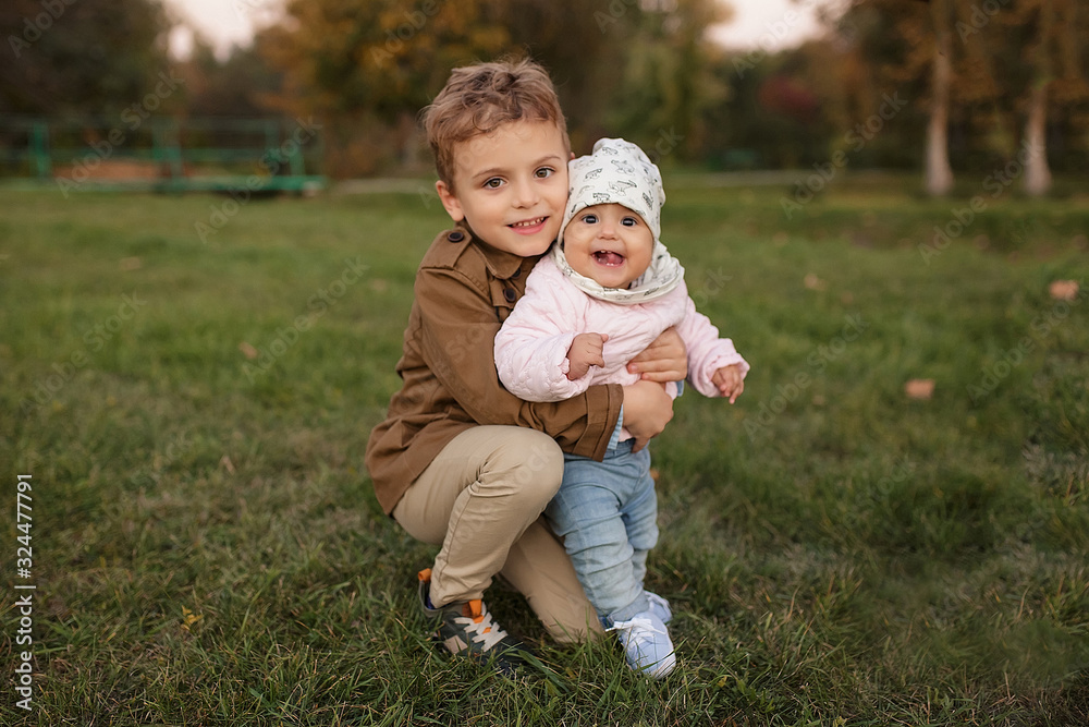 Fototapeta premium A little boy dressed in a brown coat smile and hug a his sister
