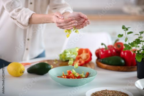 Female hands pouring light green salad into a deep plate.