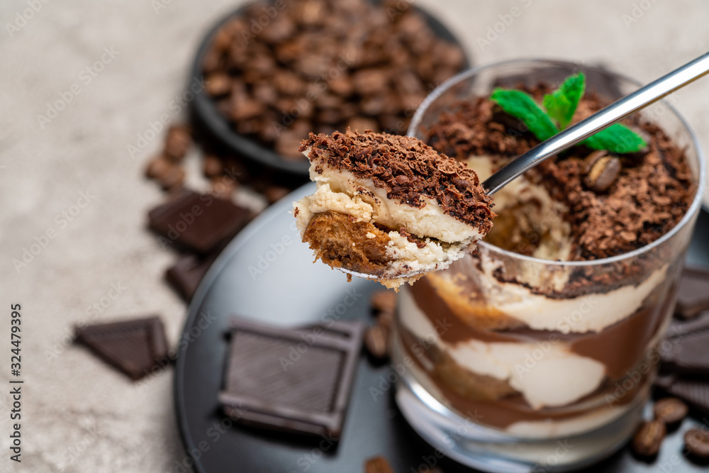 Fototapeta premium Classic tiramisu dessert in a glass cup, pieces of chocolate on concrete background