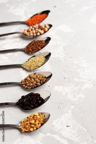 spoons with different cereals are laid out in an even row on the table. orange, black and white cereals