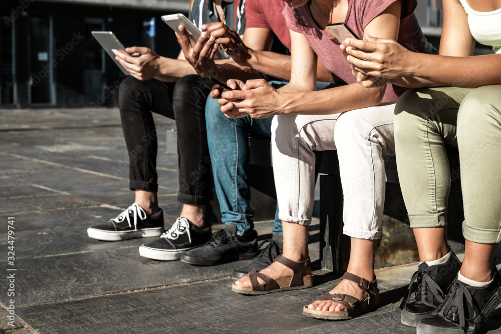 Group of people using gadgets outdoors. Anonymous men and woman sitting on bench outside, using mobile phones and tablets. Wireless technology concept