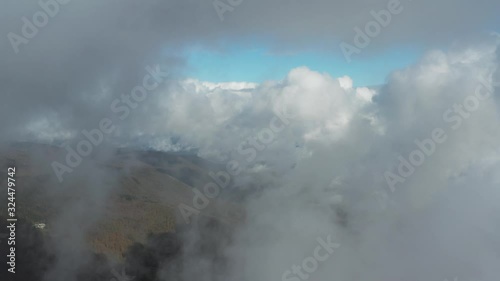 Scenic view above clouds while passing through fluffy clouds with autumn forest and blue sky in the background. Slow motion. photo