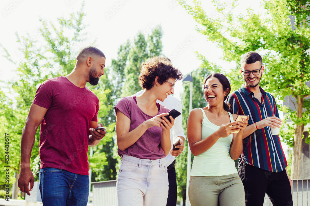 Happy joyful friends with smartphones discussing funny news. Men and women walking together outside, using mobile phones, chatting and laughing. Gadgets using concept