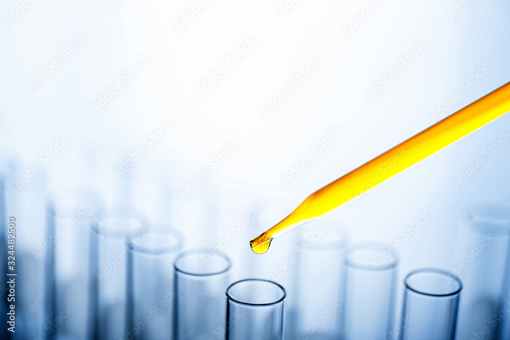 Dropping yellow chemical liquid or essential oil to test tube on white background, lab research and development concept.	