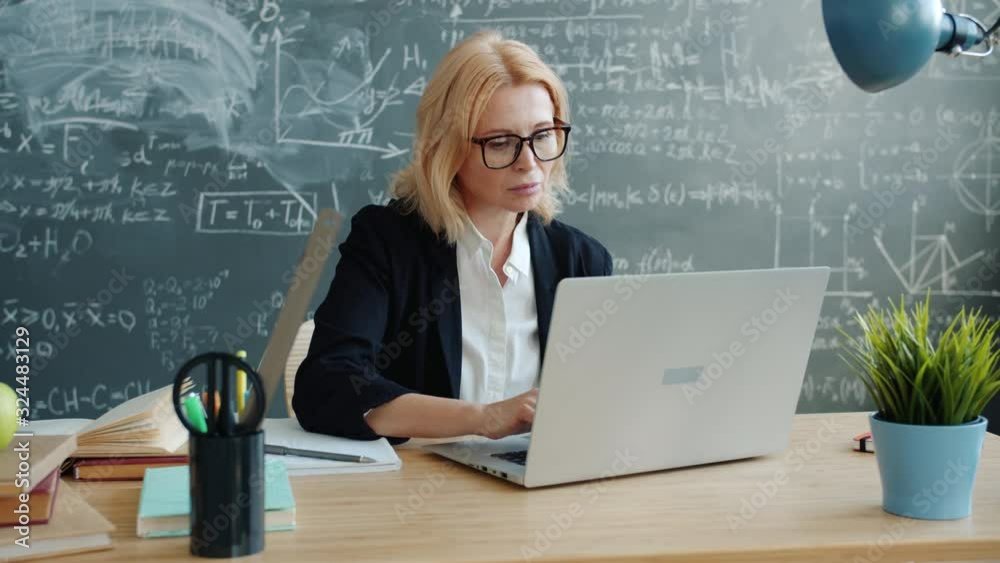 Mature woman is using laptop in class working online typing sitting at desk alone concentrated on work. Modern technology and communication concept.