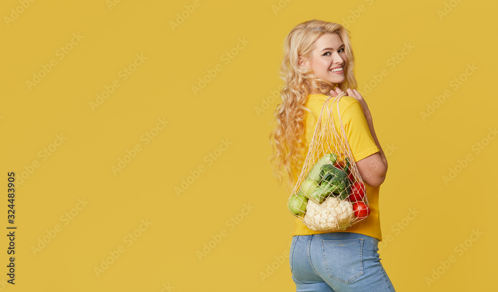 Young woman hold a string bag full of organic vegetables on yellow background. Zero waste concept. Emty space for text. Healthy Eating, Vegetarianism Young woman hold a string bag full of organic vegetables on yellow background. Zero waste concept. Emty space for text. Healthy Eating, Vegetarianism