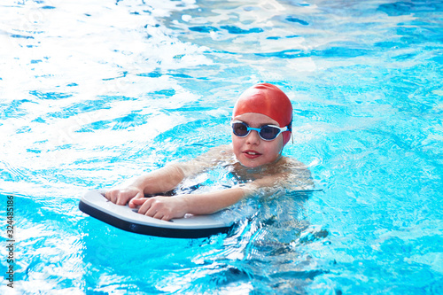 Joyful smiling boy swimmer in a cap and Goggles learns professional swimming in the swimming pool in gym close up