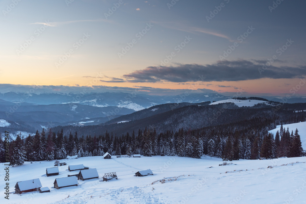 Charming snow-capped houses on a mountain Carpathian mountain valley, with magnificent views of peaks in winter.