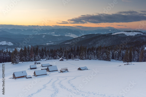 Charming snow-capped houses on a mountain Carpathian mountain valley, with magnificent views of peaks in winter.