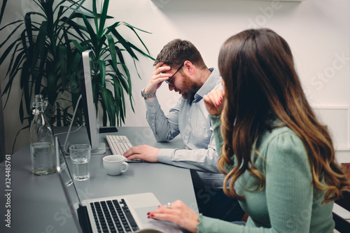 Young male having headache at work. His colleague trying to help.	