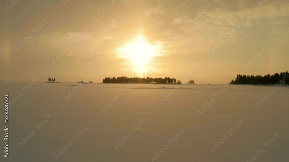 A drone shot flying towards the sun over a frozen lake in northern Sweden A drone shot flying towards the sun over a frozen lake in northern Sweden