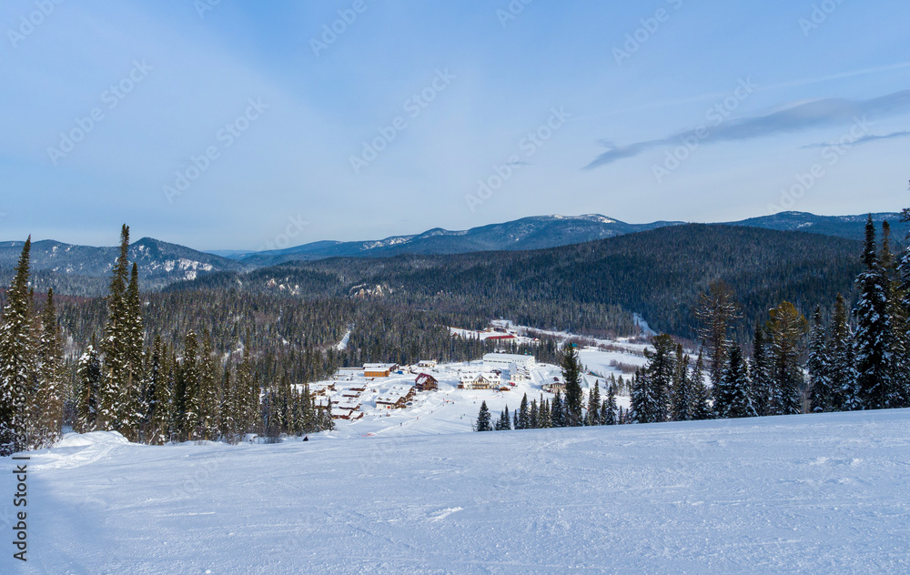 View from the top of the mountain to the ski resort. Siberian winter taiga. Mountain valley