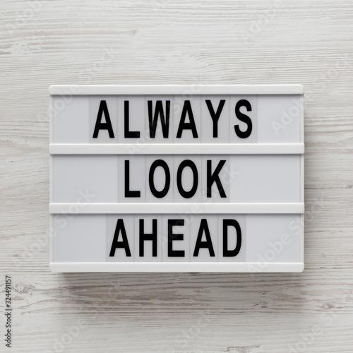 'Always look ahead' words on a modern board, clipboard with blank sheet of paper on a white wooden background, top view. Overhead, from above, flat lay.