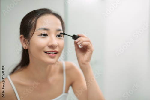 Young asian woman applying mascara in bathroom